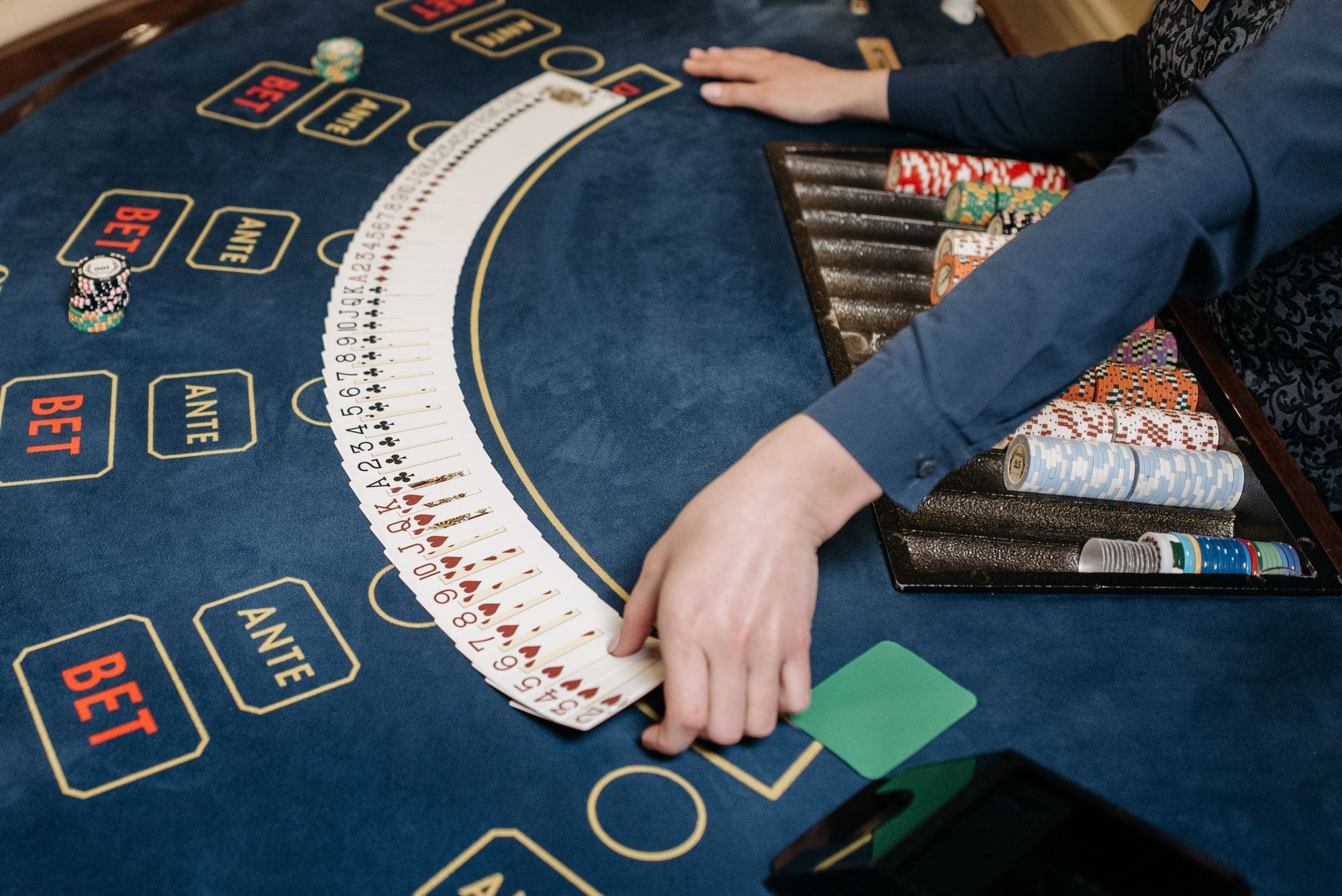A dealer fanning a full deck of cards in an arc across the blue baize of a card table beside stacked chips